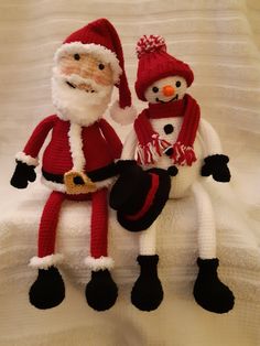 two knitted snowmen sitting next to each other on a white blanket with black feet