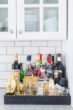 a black tray filled with bottles and glasses on top of a kitchen counter next to white cabinets