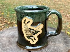 a green and black coffee mug sitting on top of a tree stump