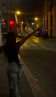 a woman is walking down the street with her arms in the air and pointing at something