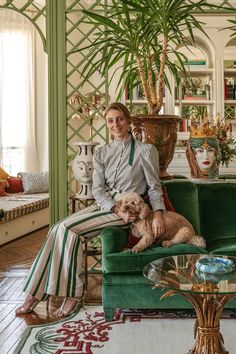 a woman sitting on a green couch with a dog in her lap next to a potted plant