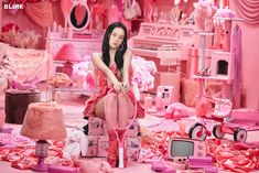 a woman sitting on top of a pink chair in a room filled with furniture and accessories