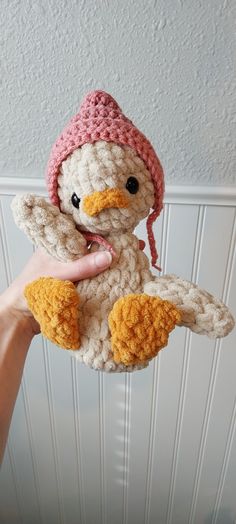 a hand holding a small crocheted stuffed animal with a pink hat on it's head