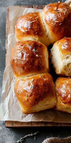 freshly baked bread rolls sitting on top of wax paper with sprigs of rosemary