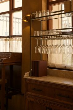 wine glasses are lined up on a shelf next to a window with curtains and windowsills