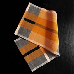 two orange and black plaid napkins on top of each other in front of a black background