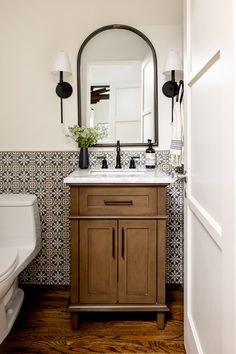 a white toilet sitting next to a bathroom sink under a large mirror on top of a wooden cabinet