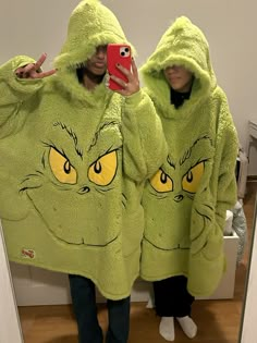 two people in green cat costumes taking a selfie with their cell phone while they both wear matching hoodies