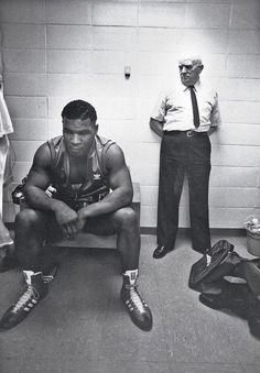 a man sitting on a bench next to another man in a locker room with other men