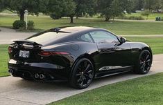 a black sports car is parked on the side of the road in front of some grass