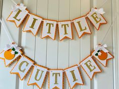 a little cutie banner hanging on the wall with an orange and white ribbon around it