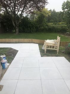 an empty patio in the middle of a yard with a bench and trash can nearby