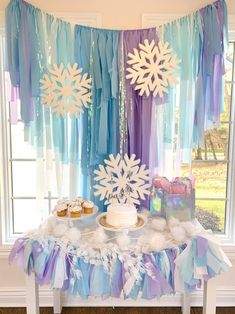 a table topped with cake and cupcakes under snowflaked paper decorations