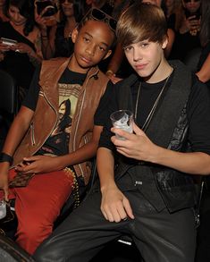 two young men sitting next to each other at a party, one holding a cell phone