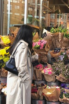 a woman standing in front of a flower shop with lots of flowers on display behind her