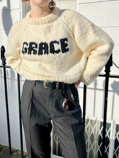 a woman standing in front of a fence wearing a sweater with the word grace written on it