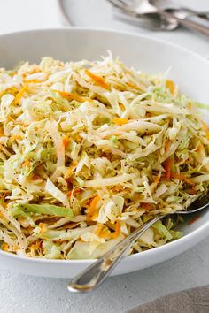 a white bowl filled with coleslaw on top of a table next to silverware