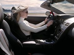 a woman sitting in the driver's seat of a car with her hand on the steering wheel