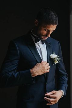 a man in a tuxedo adjusts his flower on his lapel collar