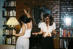 two women standing in front of a brick wall with bookshelves on either side