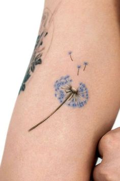 a woman's arm with a dandelion tattoo on the back of it