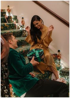 a man kneeling down next to a woman holding a present in front of her on the stairs