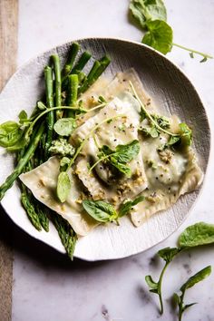 a white plate topped with ravioli and asparagus on top of a table