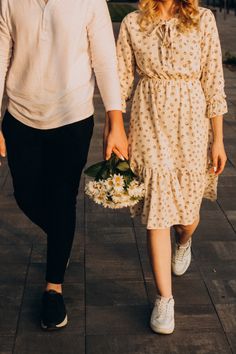 a man and woman are walking down the street holding hands with flowers in each hand