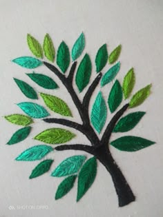 a green and black tree with leaves on it's trunk is embroidered onto a white piece of cloth