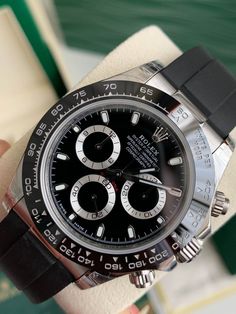 Die Rolex auf dem Bild ist eine Rolex Cosmograph Daytona.  Dieses Modell ist insbesondere am schwarzen Zifferblatt mit silbernen Hilfszifferblättern, der schwarzen Keramiklünette und dem Oysterflex-Armband zu erkennen, die bei einigen modernen Daytona-Referenzen wichtige Designelemente darstellen.
Aufgrund dieser Merkmale ist diese Rolex höchstwahrscheinlich aus der Oyster Perpetual Cosmograph Daytona 116519LN-Serie.  Die Referenznummer für dieses spezielle Modell wäre 116519LN, mit einer schwarzen Keramiklünette und einem schwarzen Zifferblatt mit einem Oysterflex-Armband. Luxury Black Chronograph Watch With Tachymeter, Classic Black Chronograph Watch With Tachymeter, Luxury Black Watch Accessories With Analog Display, Classic Black Chronograph Watch With Chronometer, Classic Black Chronograph Watch With Subdials, Timeless Black Chronograph Watch With Tachymeter, Classic Black Watch Accessories With Tachymeter, Timeless Black Automatic Chronograph Watch, Luxury Black Chronometer Watch Accessories