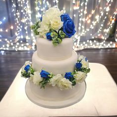 a three tiered cake with blue and white flowers on the top is sitting on a table