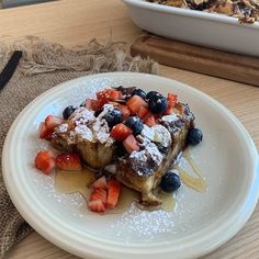 a white plate topped with french toast covered in berries and powdered sugar next to a bowl of granola