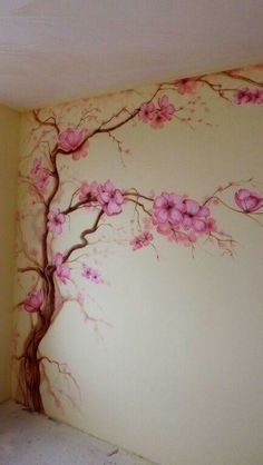 a room with a tree painted on the wall and pink flowers in the corner next to it