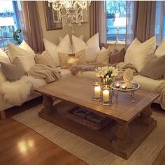 a living room filled with lots of white couches and pillows on top of a hard wood floor