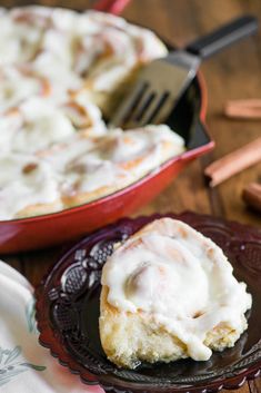 a cinnamon roll with icing on a plate next to a pan of cinnamon rolls