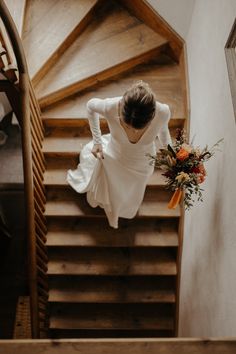 a woman in a white dress is walking down the stairs with flowers on her hand