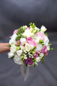 a bridal bouquet with pink and white flowers is held by someone's hand