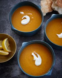 three blue bowls filled with soup next to a slice of lemon on a black surface