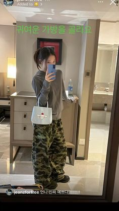 a woman taking a selfie with her cell phone in a hotel room while wearing camo pants