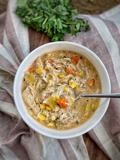 a bowl of chicken noodle soup on a striped cloth with a spoon in it