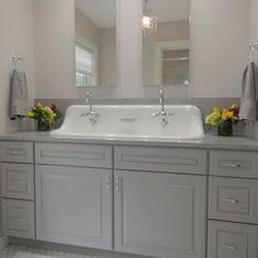 a white sink sitting under a large mirror next to two sinks in a bathroom with gray cabinets