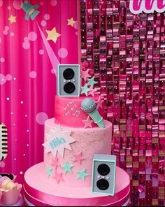 there is a pink cake with stars on it and speakers in front of the cake