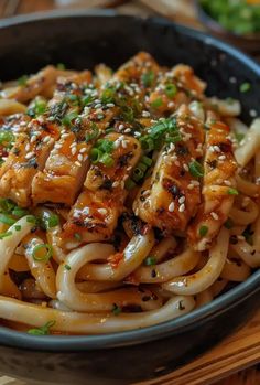 a black bowl filled with noodles and meat covered in sesame seeds, garnished with scallions