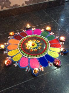 a colorful flower design on the ground surrounded by candles