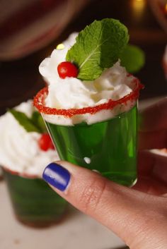 a hand holding a small green cup with whipped cream and cherries on the rim