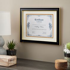 a framed certificate hangs on the wall next to a lamp and vase with flowers in it