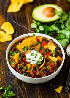 a white bowl filled with chili and tortilla chips next to an avocado