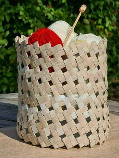 a woven basket with yarn and knitting needles in it on a wooden table next to bushes