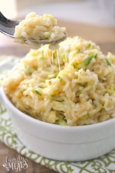 a spoon full of rice and vegetables being stirred with gravy from a white bowl