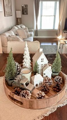 a wooden tray with pine cones and small houses on it in front of a couch